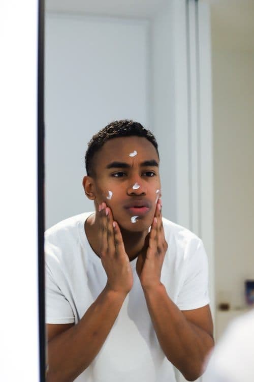 A man looking in the mirror and putting moisturiser on